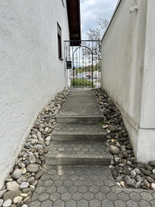 Zugang zu Tanjas Haarstudio in Eriskirch am Bodensee mit dekorativem Steingarten, gepflastertem Weg und Eisentor.